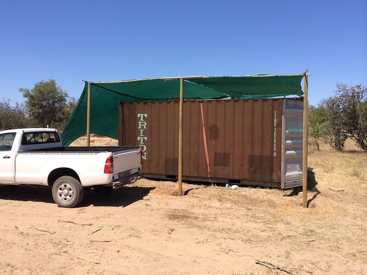 A shipping container with a makeshift canopy next to a pickup truck.