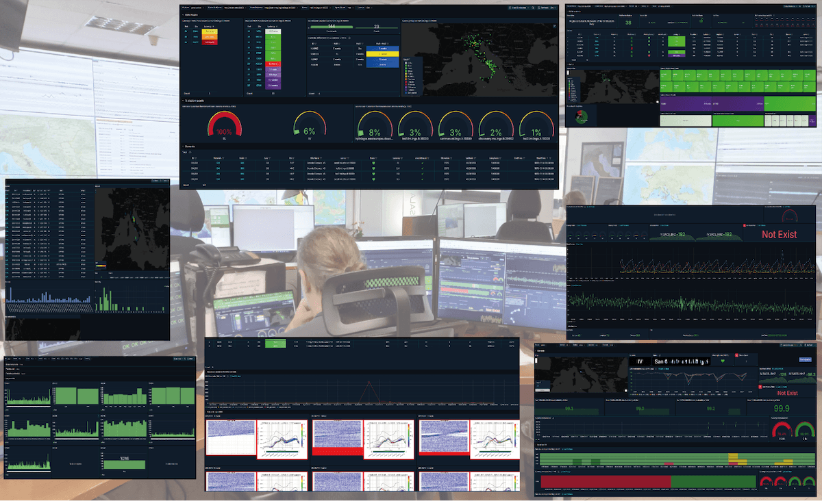 A person monitors multiple screens displaying data analytics, charts, and maps in a control room environment.
