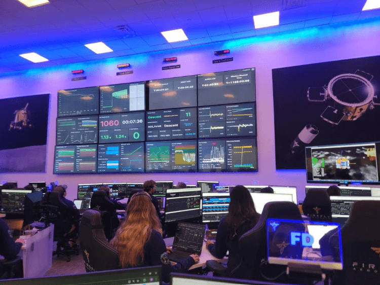 A picture of the Firefly control room, with Grafana dashboards displayed on large, wall-mounted monitors. Individuals sitting at their workstations also have Grafana dashboards on display
