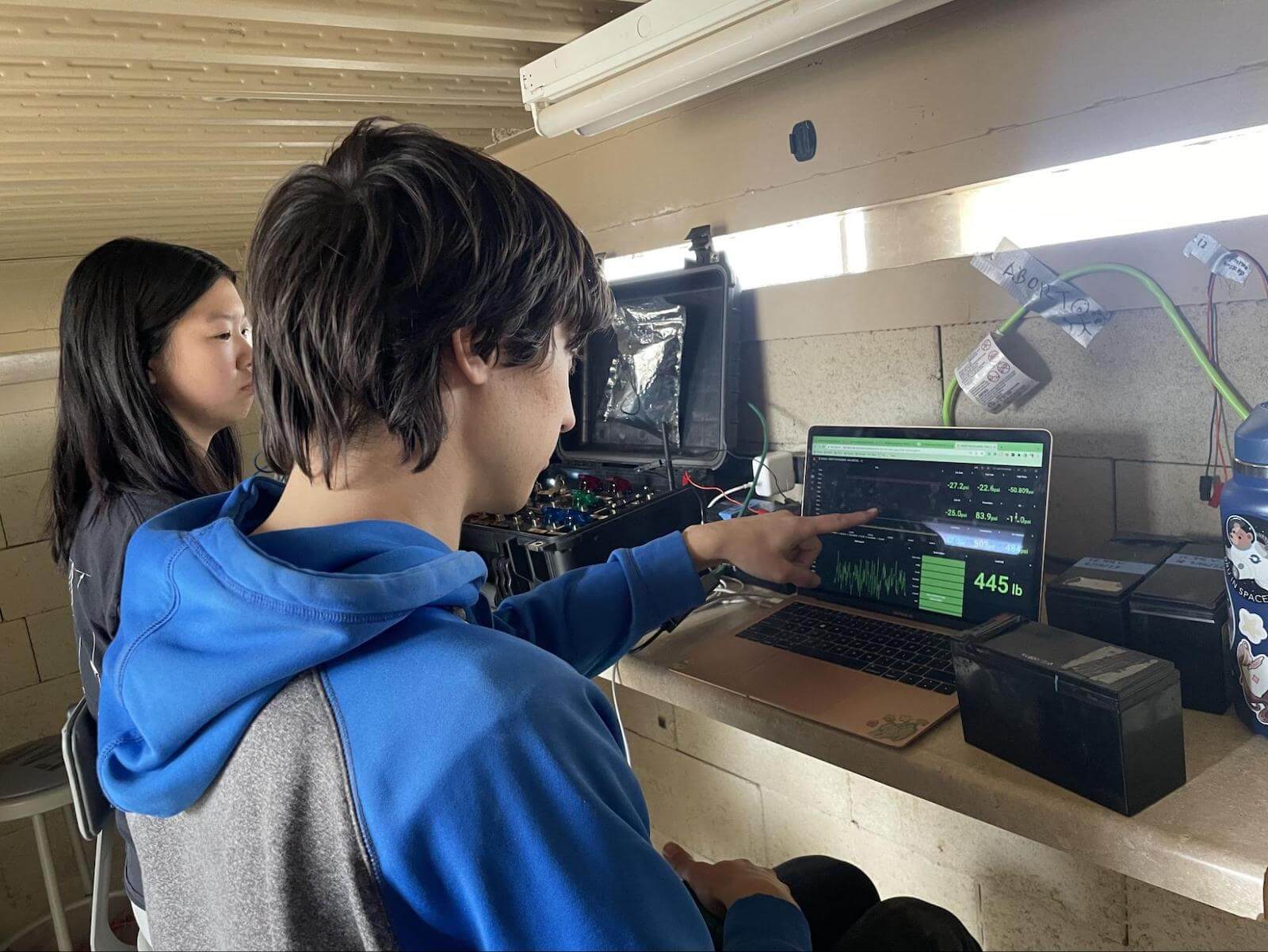 A photo of two people and one is pointing at a panel in a Grafana dashboard